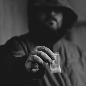 Drug dealer selling drugs junkie. Drug abuse concept and overdose concept. Mans hand holds plastic packet with cocaine powder, selective focus, black and white photo