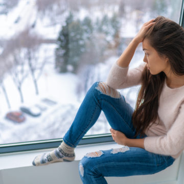 Winter depressed sad girl lonely by home window looking at cold