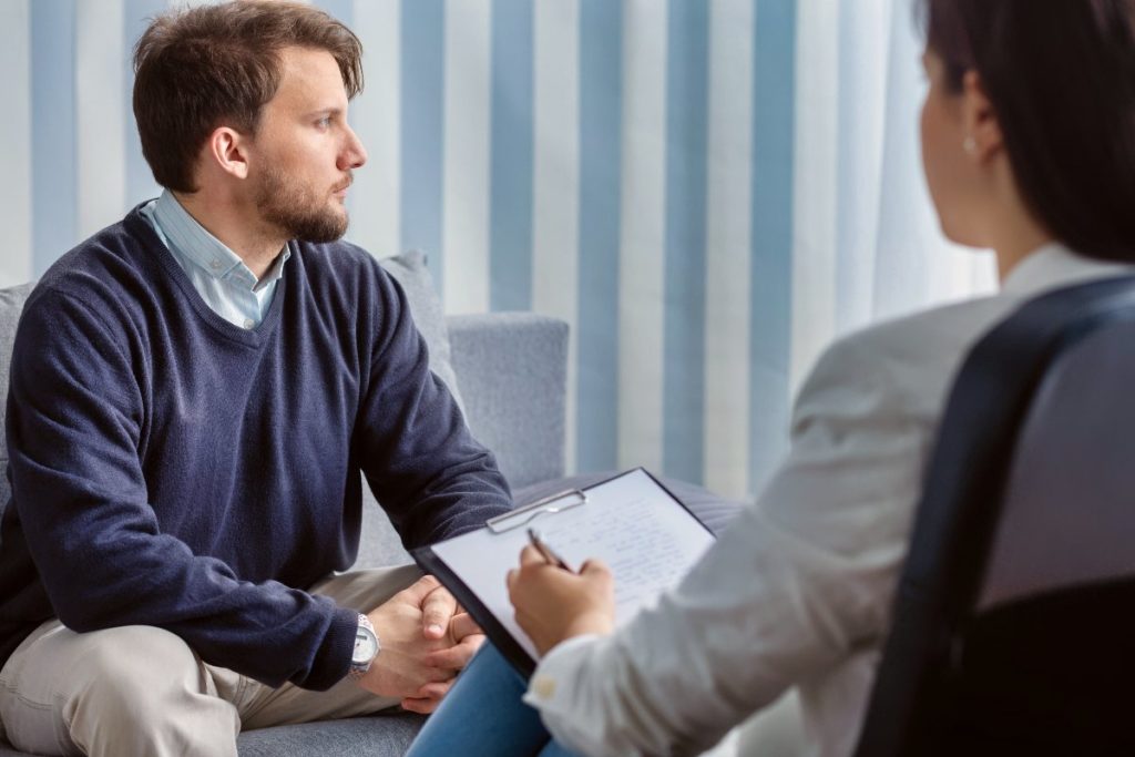 A young male patient sits across from a therapist as they review his mental health symptoms to reach a diagnosis
